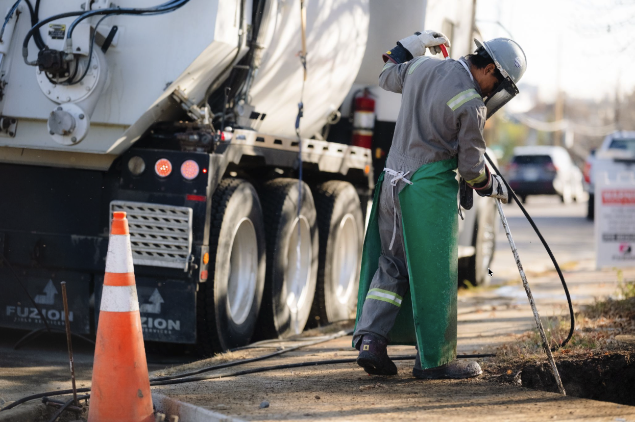 Fuzion worker performing hydrovac excavation beside a utility truck in a residential area.