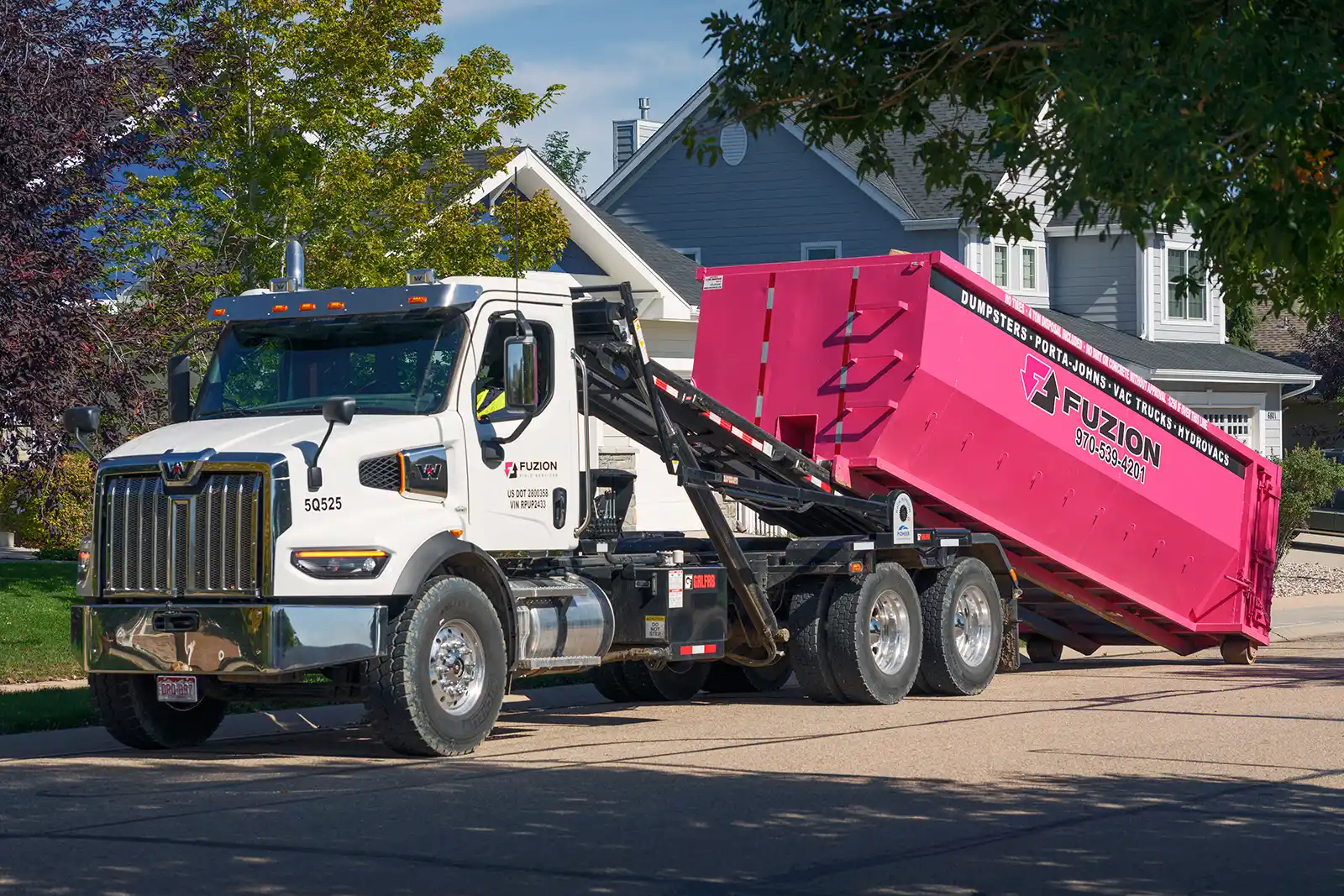 Fuzion truck placing a pink dumpster in front of a suburban home.