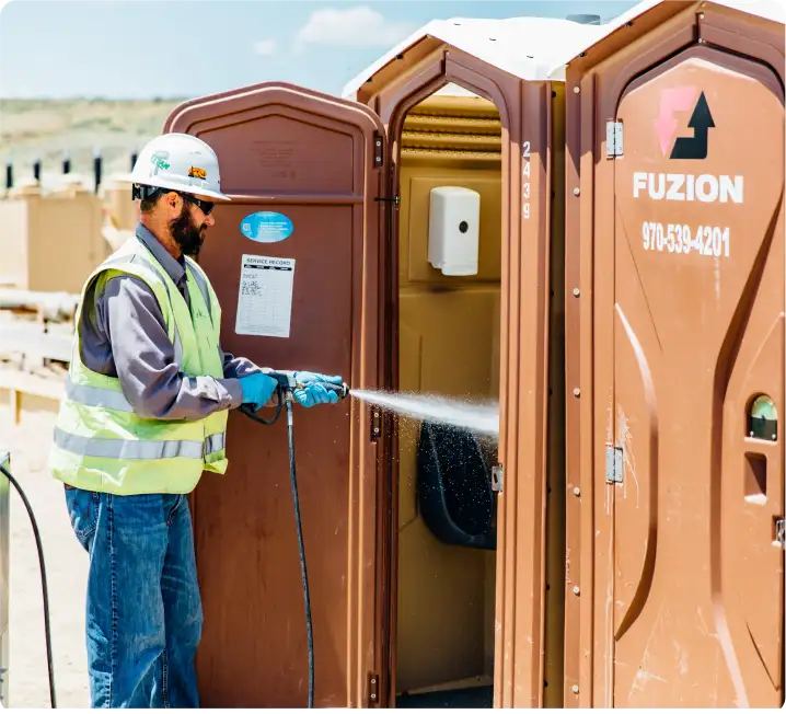 Fuzion Field Services employee cleaning a portable toilet