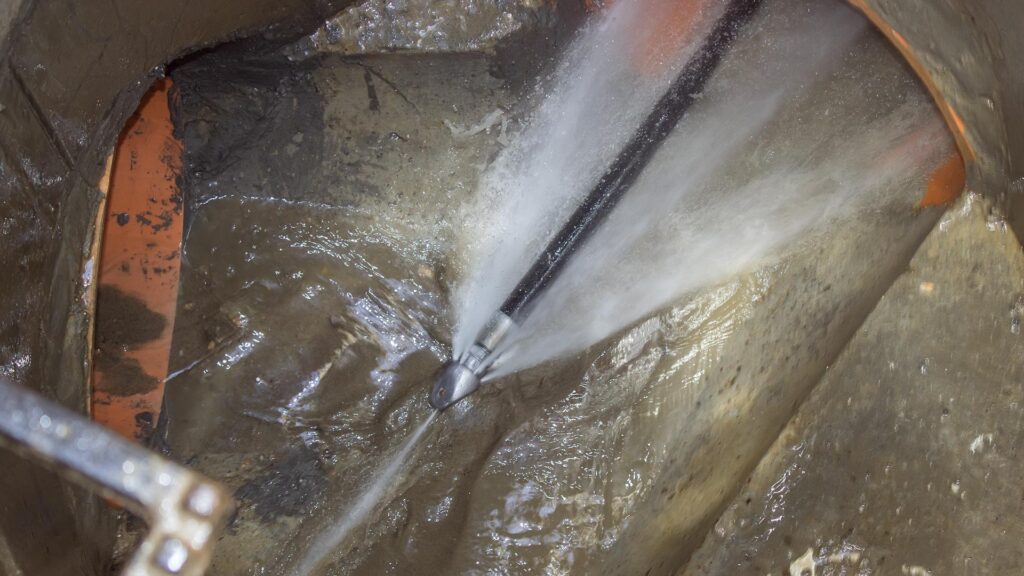 Hydro jetting nozzle spraying pressurized water to clean pipes in a commercial drainage system.