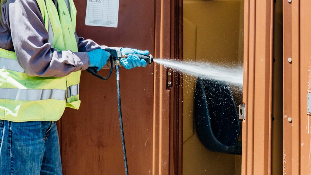 Fuzion worker cleaning a porta potty with disinfectant spray.