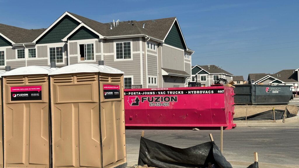 Multiple Fuzion porta potties and dumpsters on a construction site.