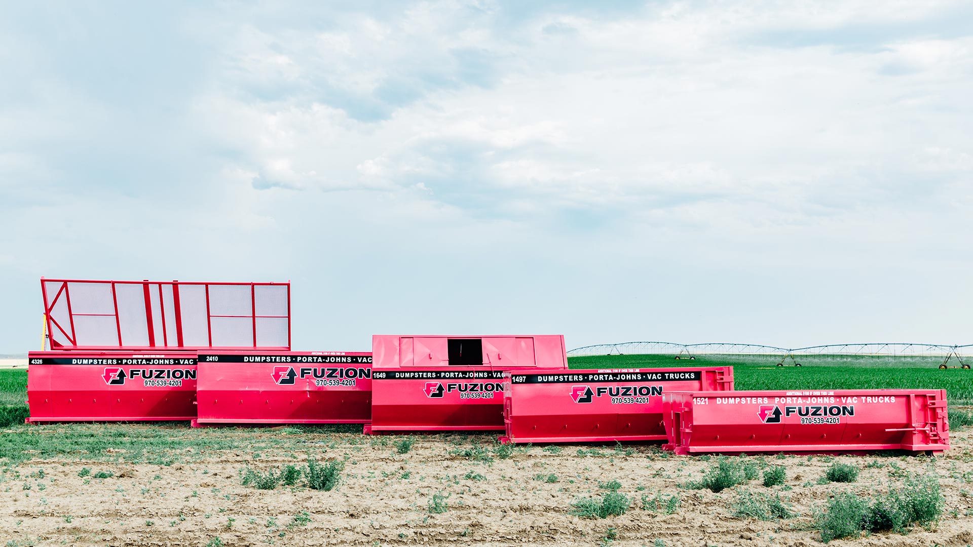 Different sized dumpster rentals lying in a field.