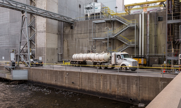 A Fuzion removal truck is parked outside an industrial plant.