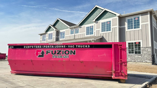 Large pink roll-off dumpster outside residential construction site.