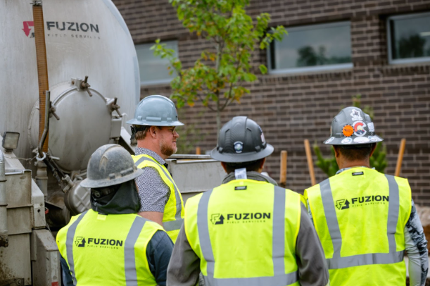 Crew members in Fuzion safety gear gather near industrial equipment during a project.
