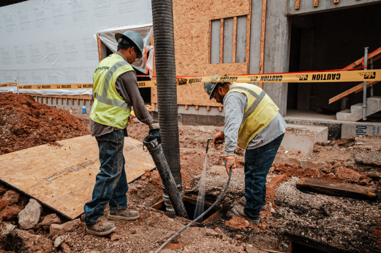 Two technicians guiding a hydro jetting hose into an access point on a construction site.