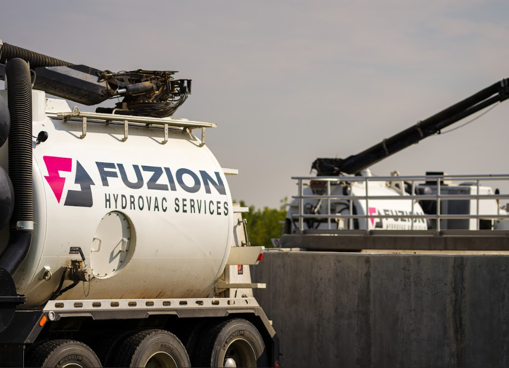 Close-up of a Fuzion Hydrovac Services truck with another in the background at a job site.
