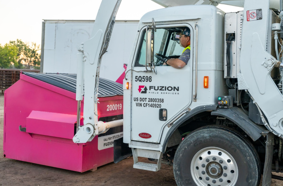 Fuzion Field Services truck operator lifts a pink dumpster during collection.