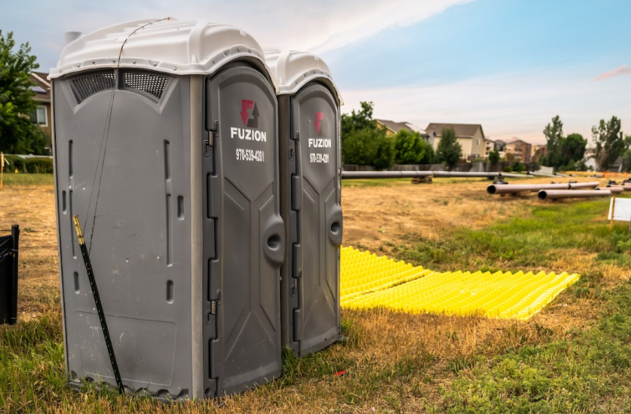Two Fuzion portable restrooms set up on a grassy construction site.