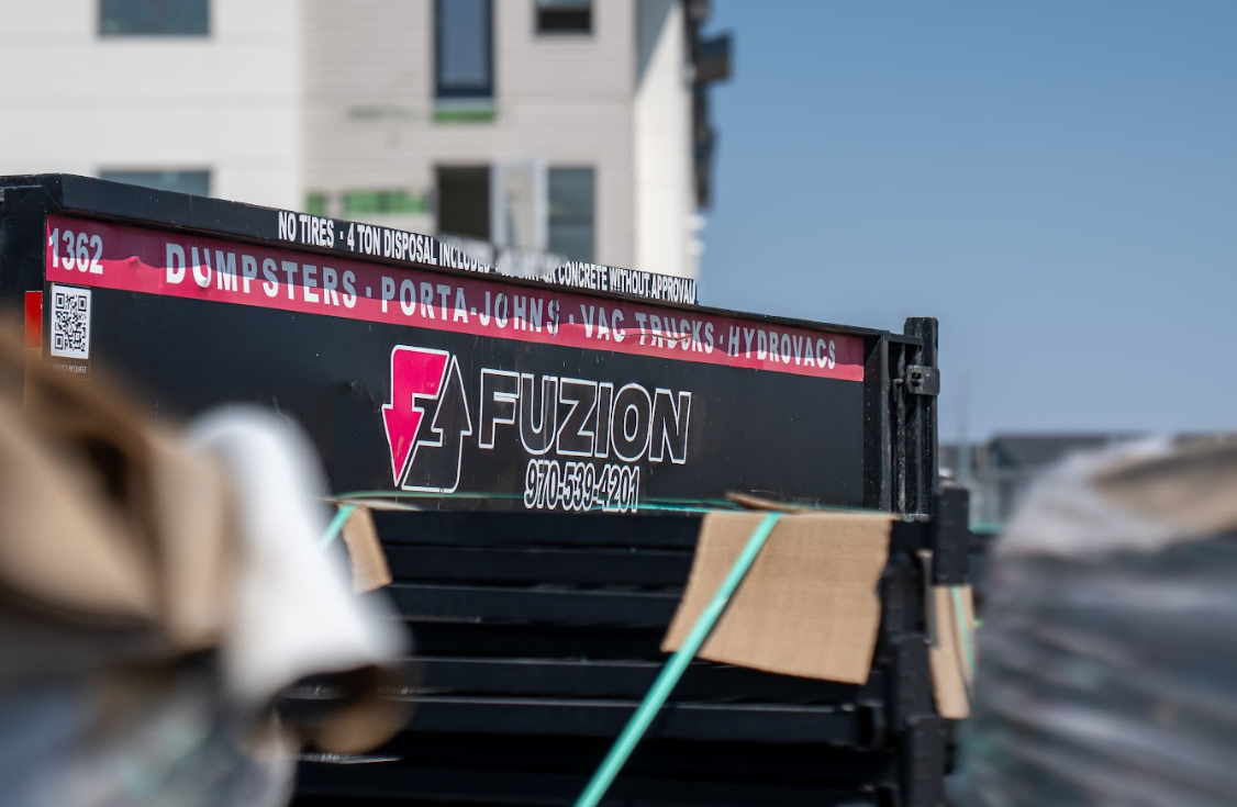 A Fuzion dumpster sits beside a home ready for renovation.