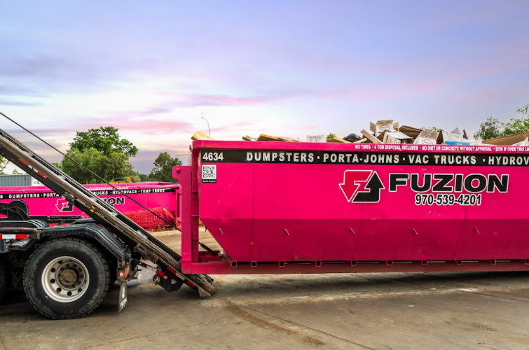 A bright pink Fuzion dumpster loaded with debris sits ready for pickup during an apartment turnover.