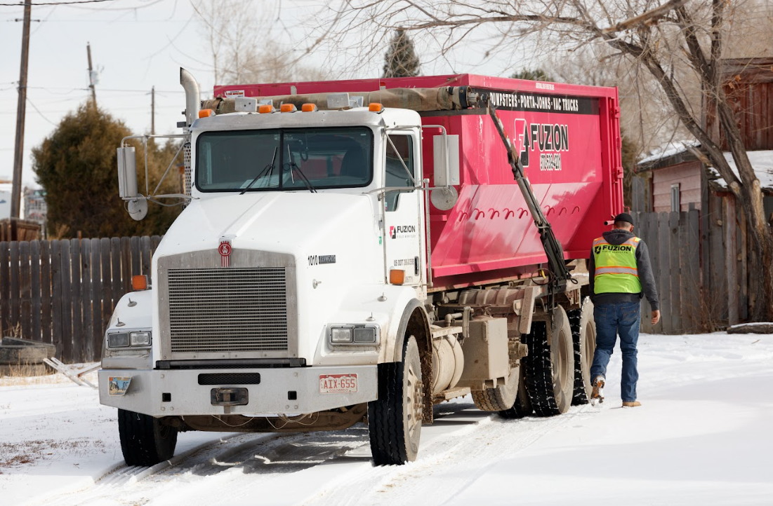 A Fuzion truck delivers a bright pink dumpster in a snowy neighborhood, showing a typical dumpster rental for home use.