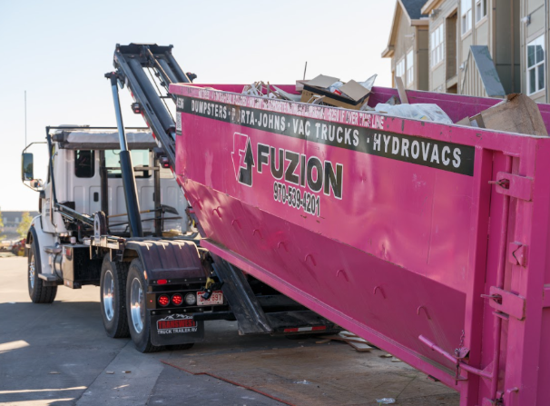 A Fuzion truck loads a pink dumpster filled with debris during an apartment turnover cleanup.