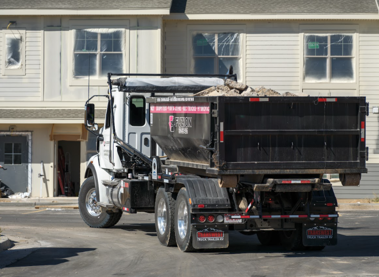 A Fuzion dump truck loaded with debris at a residential construction site.