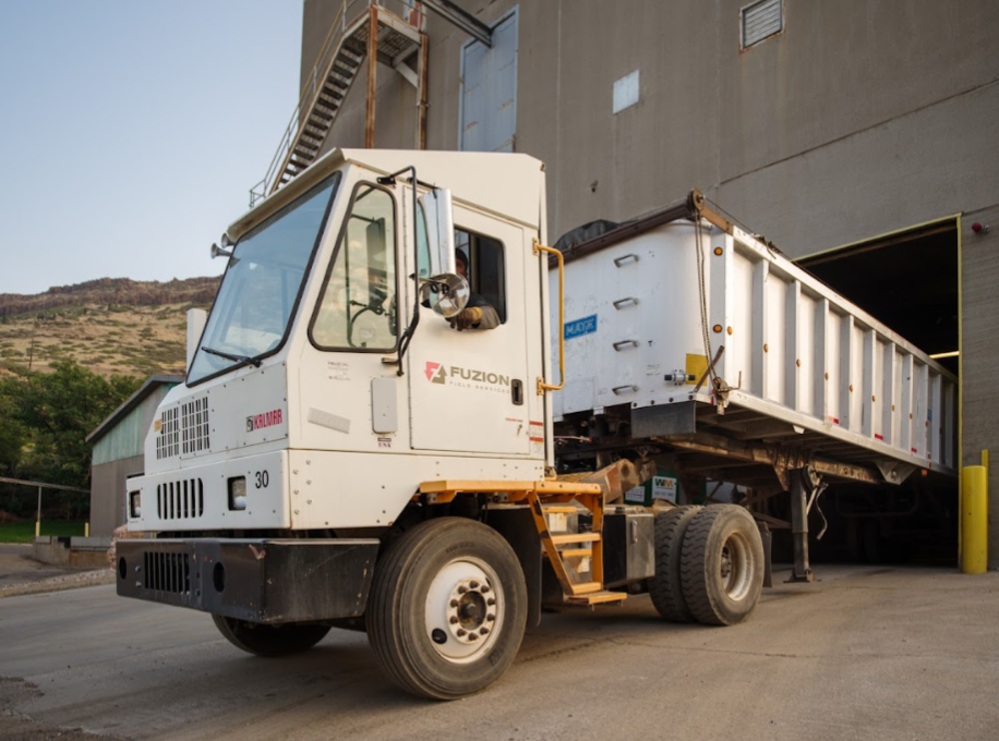 Fuzion industrial truck transporting waste materials into a large processing facility.