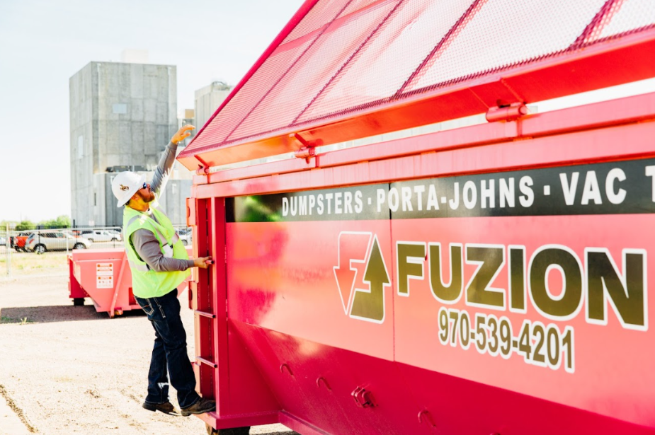 Worker securing a Fuzion dumpster lid as part of landfill diversion practices.