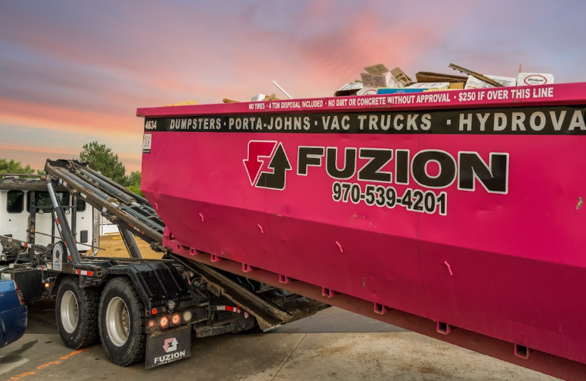 Fuzion roll off dumpster trash removal service picking up a full construction dumpster at sunset