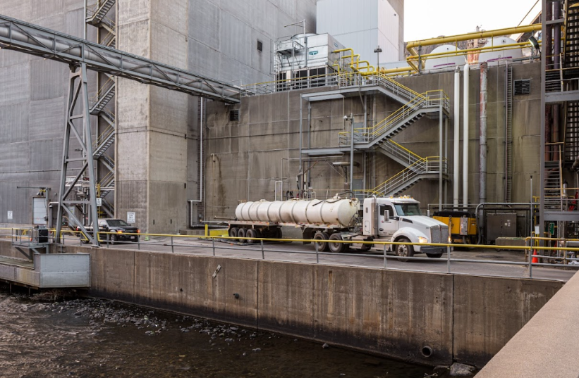 Industrial water tank cleaning truck servicing a large facility with elevated piping and storage systems.