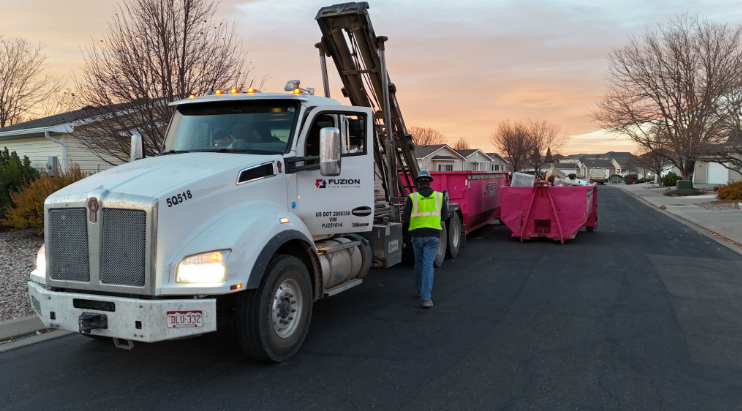 Fuzion truck delivering pink dumpsters on a residential street.