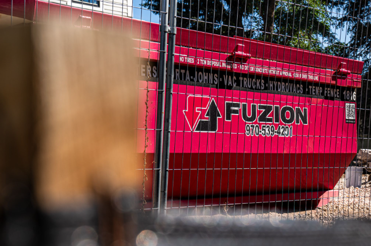 Pink Fuzion dumpster behind a temporary construction fence at a job site