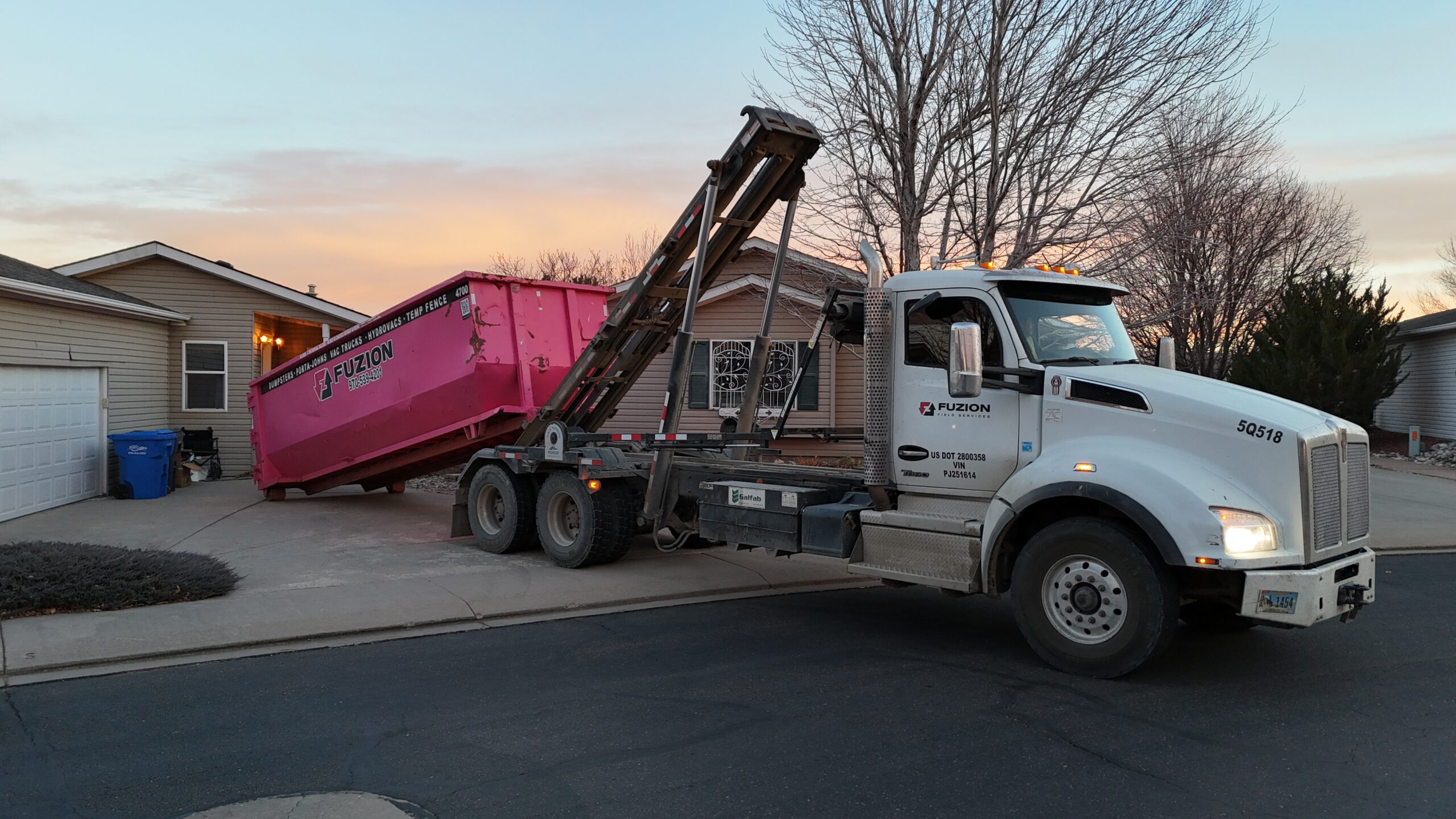 Fuzion truck placing a pink dumpster in a residential driveway