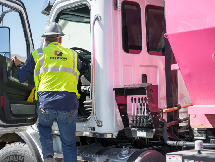 Fuzion worker climbing into a pink dumpster truck at a job site.