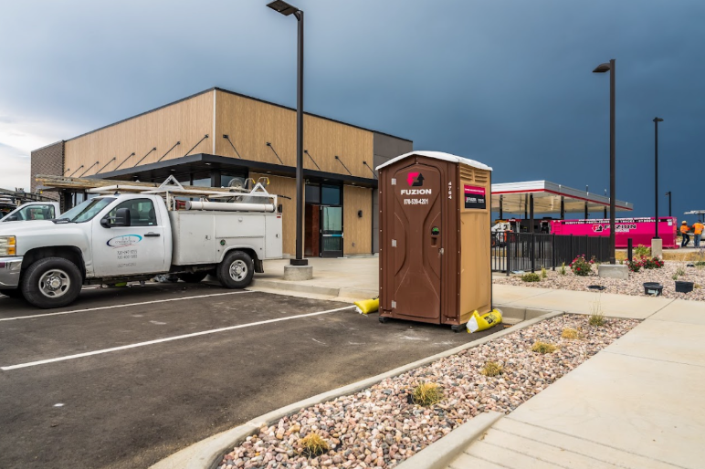 Fuzion portable toilet outside a commercial building under construction with a work truck nearby.