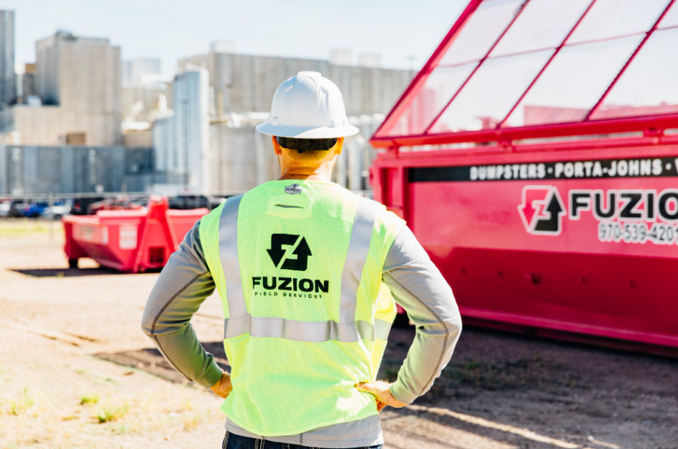 Fuzion team member standing beside a roll-off dumpster at an industrial site.