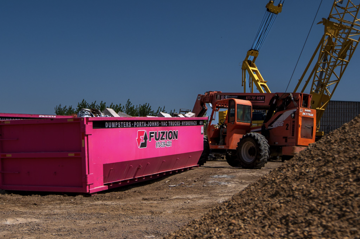 Fuzion roll-off dumpster at an active construction site with heavy equipment nearby. 