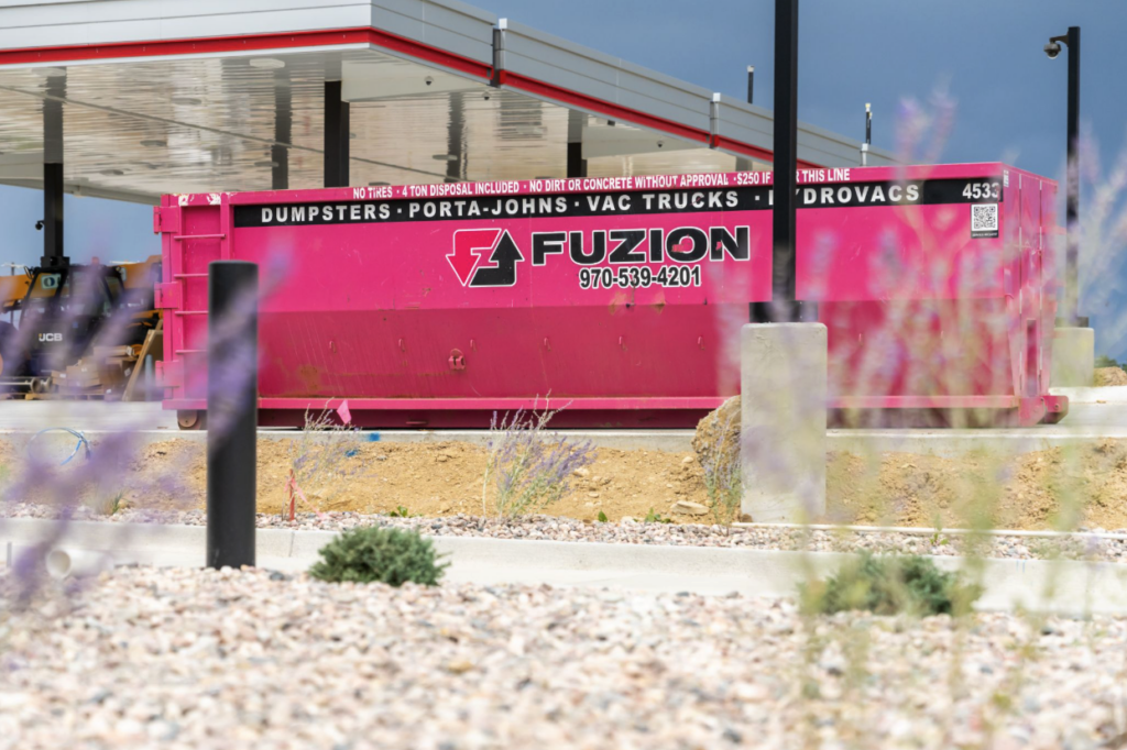 Bright pink Fuzion dumpster container positioned at an active construction site.
