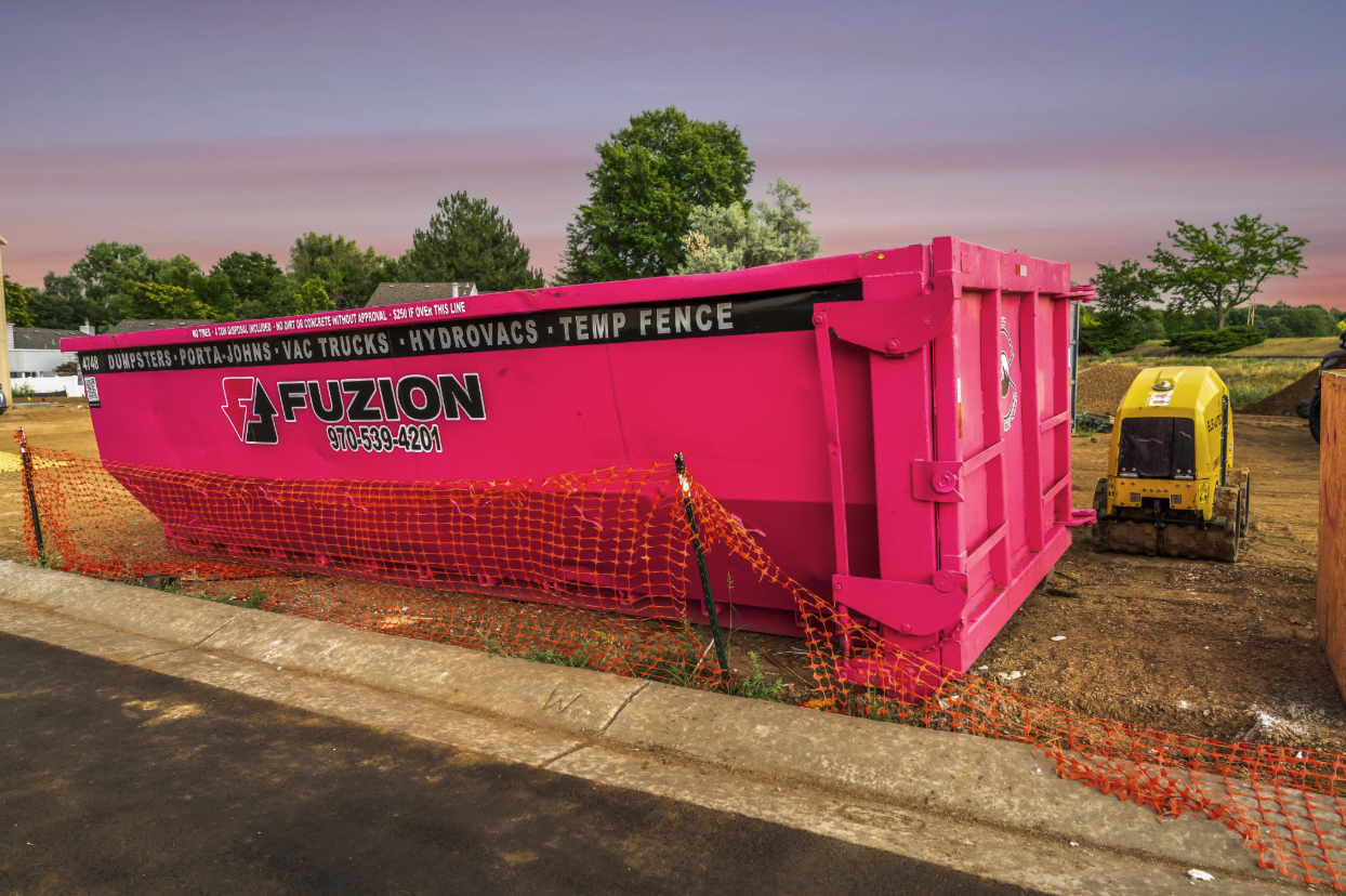 Bright pink Fuzion dumpster container placed at a residential construction site.