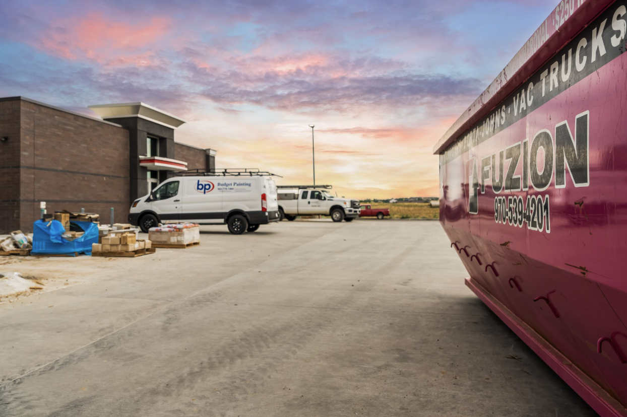 Fuzion dumpster positioned outside a commercial construction site during an evening sunset.