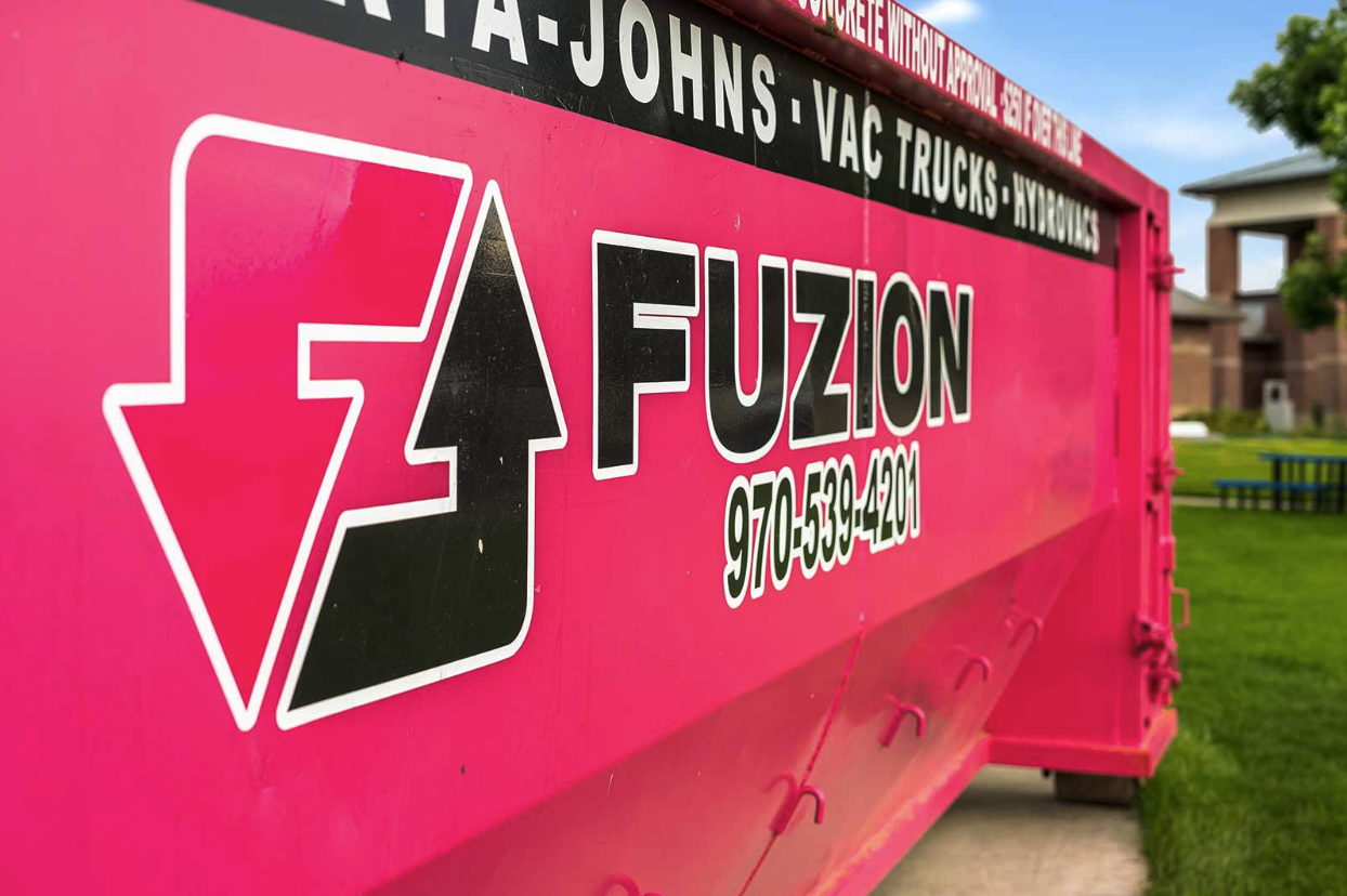 Close-up of a bright pink Fuzion dumpster container positioned at a residential construction site.
