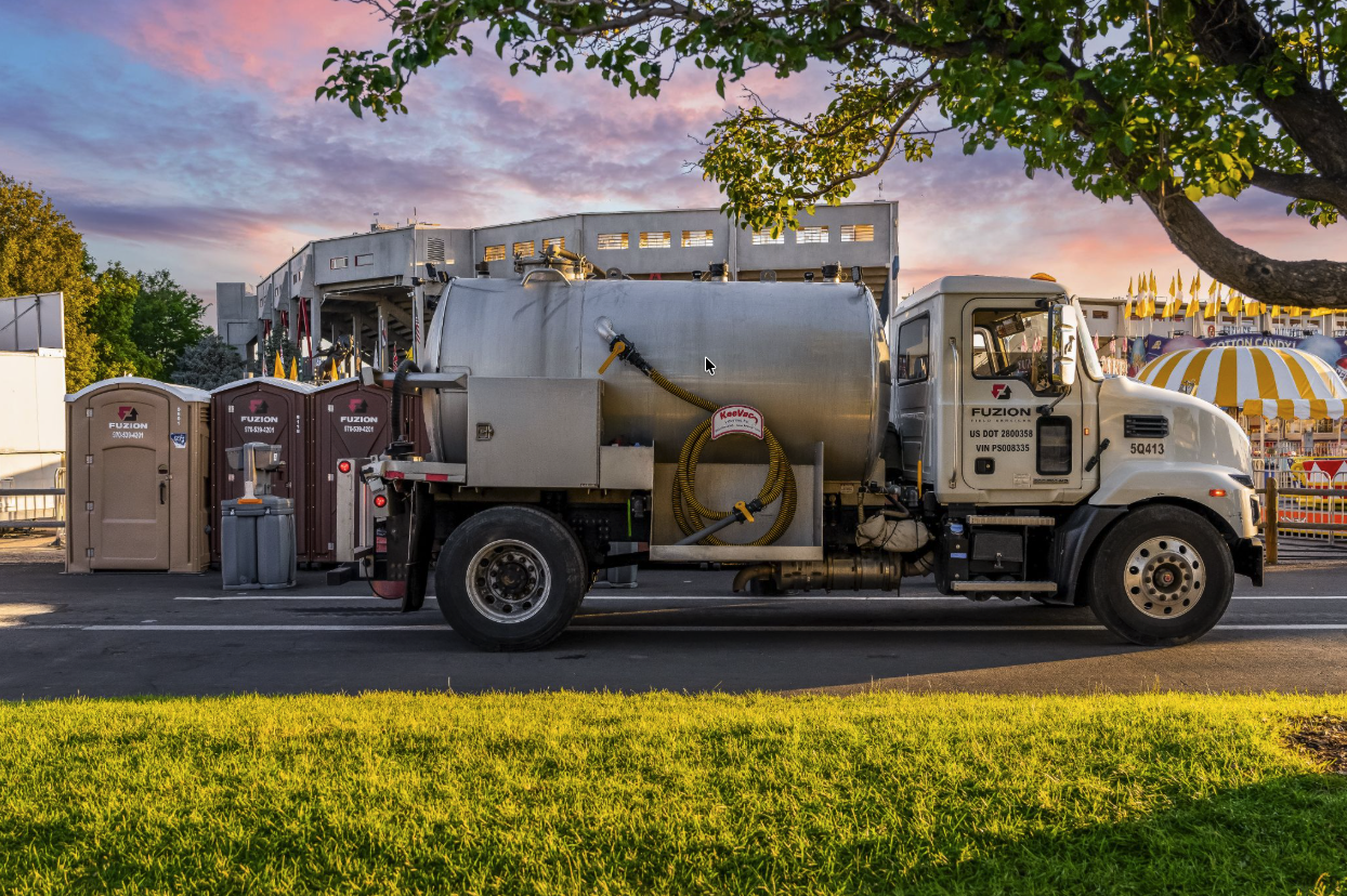 Fuzion vacuum truck and portable restrooms set up at an outdoor event location during sunset.