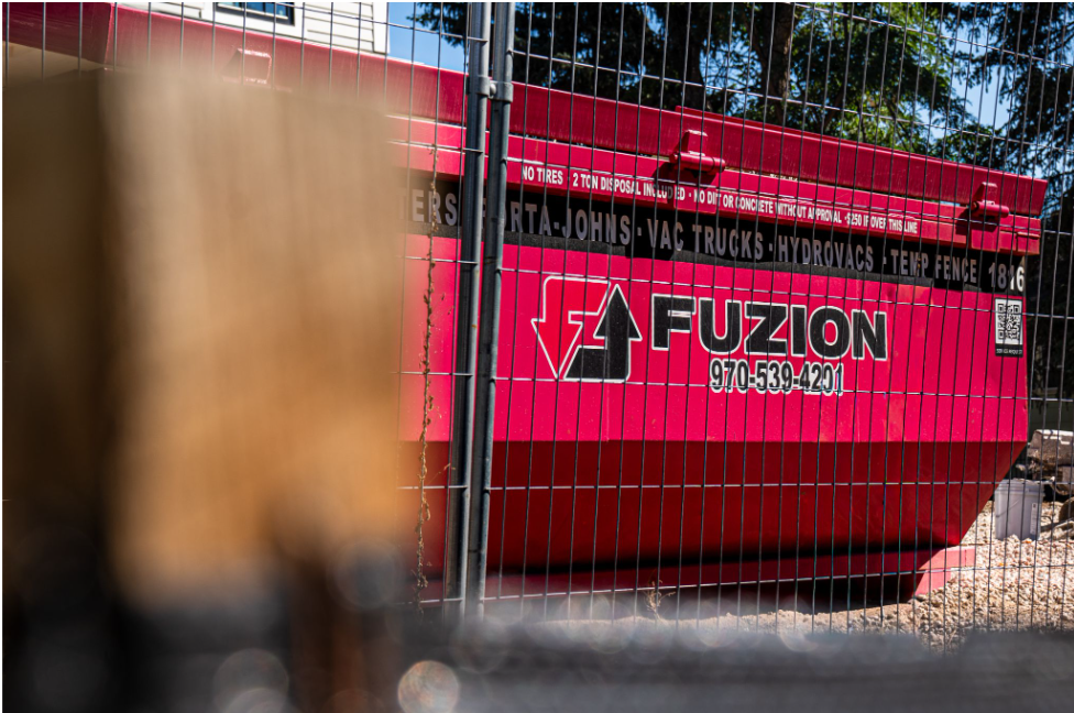 Fuzion roll-off dumpster positioned behind temporary fencing at a construction site.